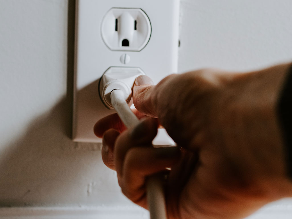 Hand pulling electrical plug from wall socket