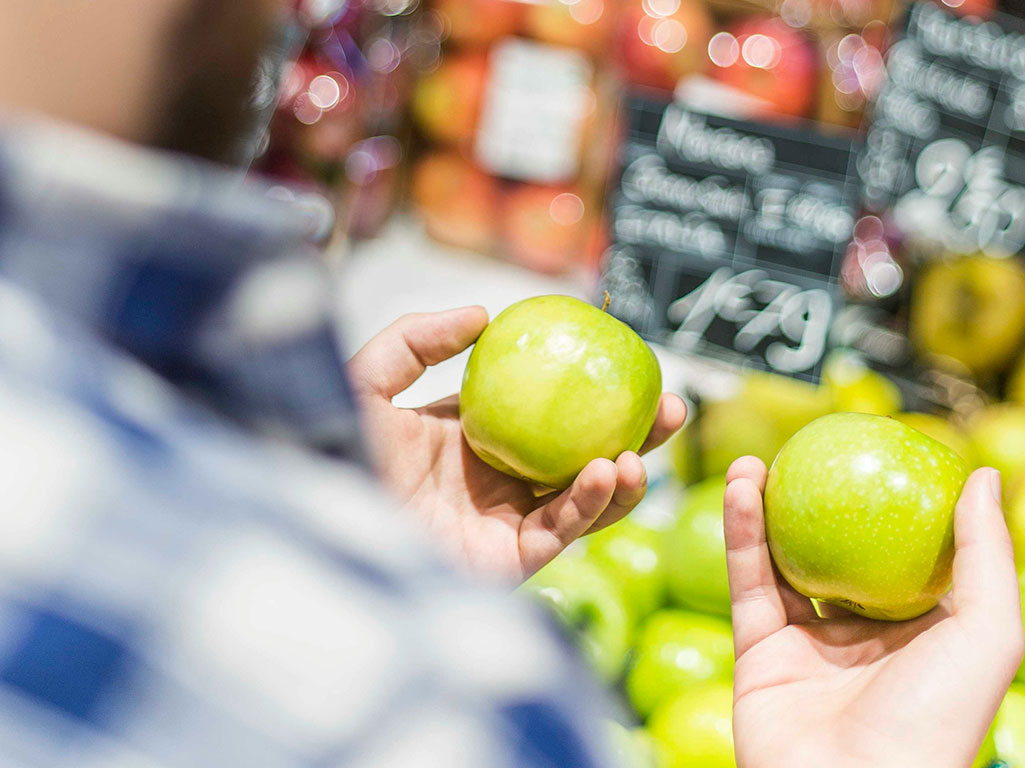 man choosing between two apples at grocery store