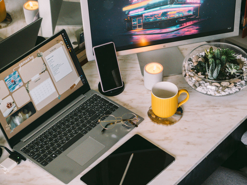 Tidy office desk with computers, tablet, and cell phone